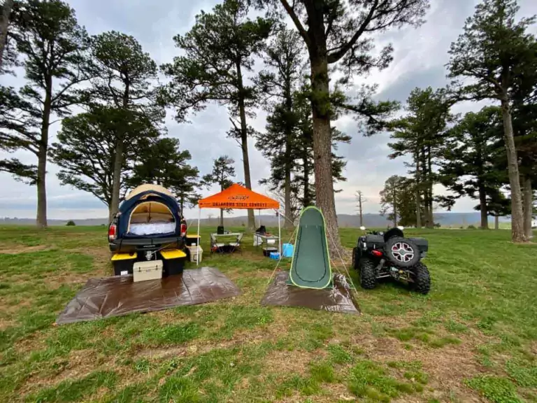 tress, grass, camping location with trucks, cars, and tents and portable camping toilet for trucks
