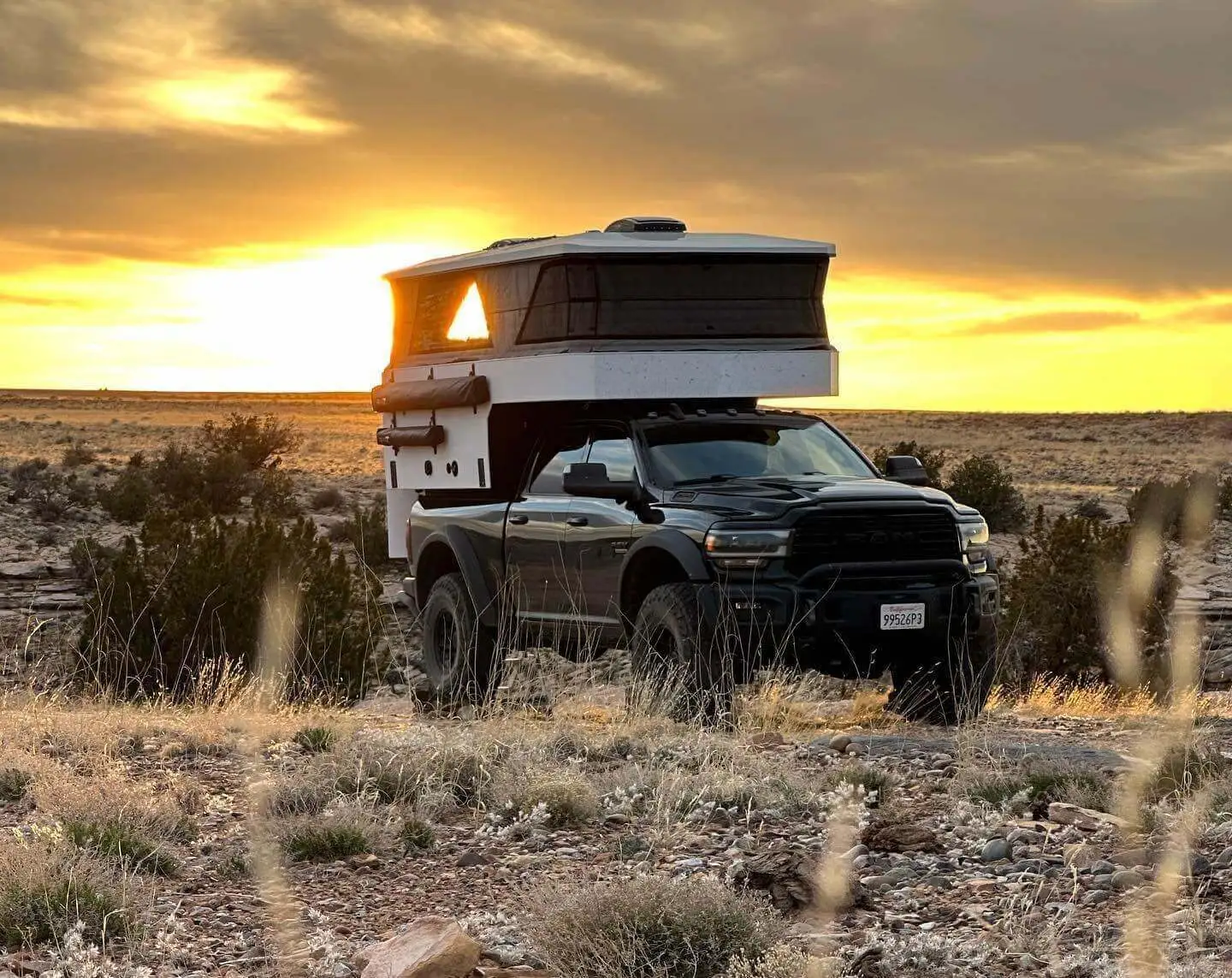 pop up truck camper on a black truck in a dessert site with sunset view