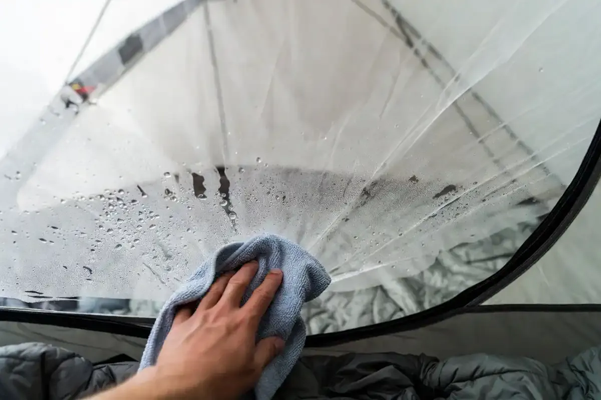 Best Lightweight Truck Campers (2026): 15 Picks That Won't Overload Your Truck 8 Hand wiping condensation droplets from the inside of a pop-up camper tent wall