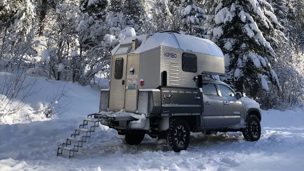 Best Lightweight Truck Campers (2026): 15 Picks That Won't Overload Your Truck 5 Kimbo aluminum hard-side truck camper covered in snow at a winter campsite