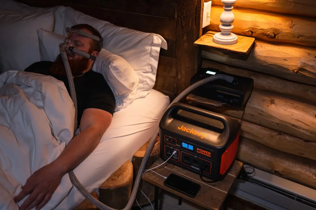 CPAP machine powered by a Jackery power station on a bedside table at night