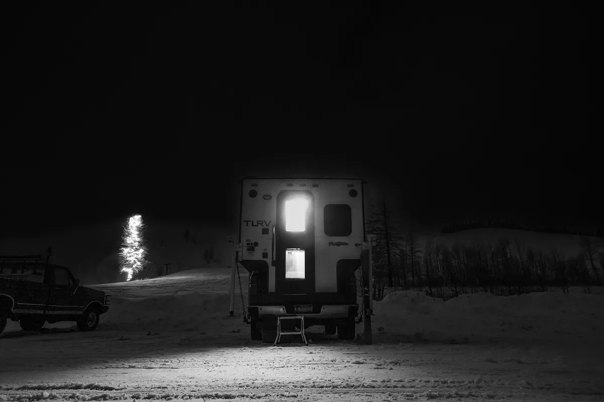 Best Truck Camper for Full-Time Living in 2026: 7 Rigs Compared 2 Hard-side truck camper parked in snow at night with interior light glowing through the door, pine trees behind