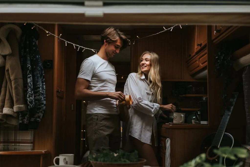 Best Truck Camper for Full-Time Living in 2026: 7 Rigs Compared 7 Couple preparing dinner together in a warmly lit compact camper kitchen at night with string lights