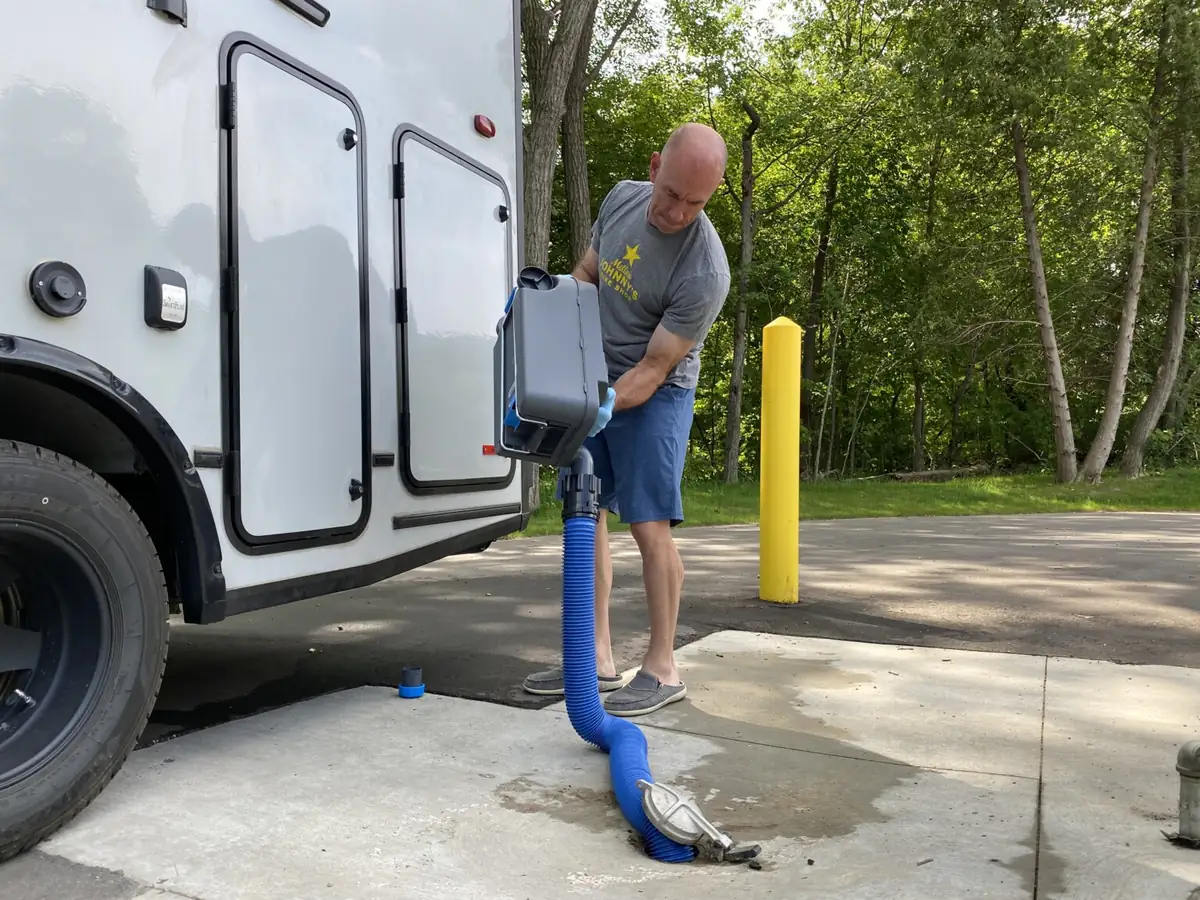Man emptying a wheeled cassette toilet tank into an RV dump station drain