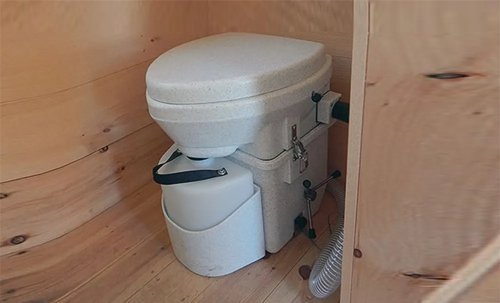 Natures Head composting toilet installed in a small wooden camper bathroom with vent hose visible