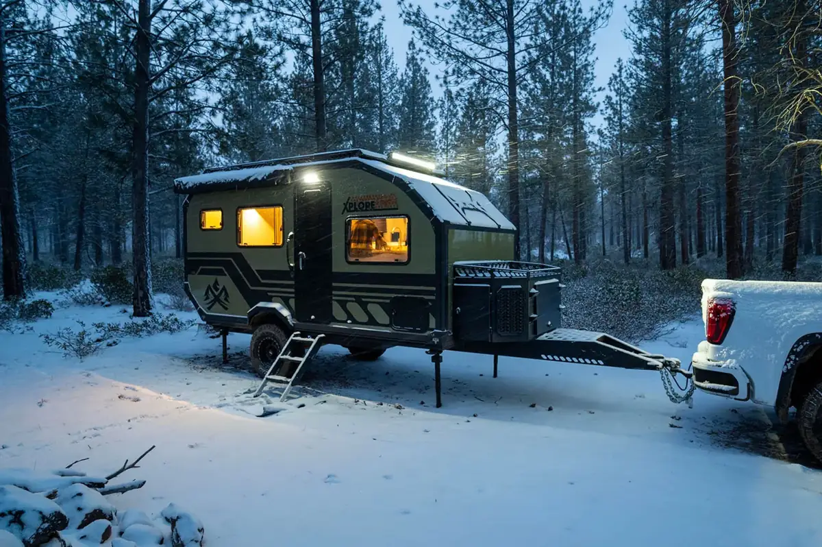 Camper glowing with warm light at a snowy winter campsite in the forest at dusk