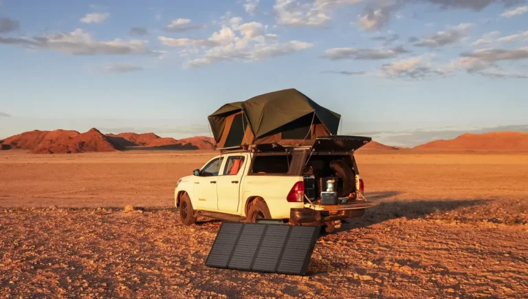 Portable power station on a pickup tailgate with rooftop tent and solar panel at a campsite