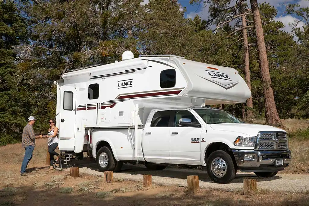 Best Truck Camper for Full-Time Living in 2026: 7 Rigs Compared 1 Lance hard-side truck camper mounted on a white Ram 3500 dually pickup truck at a wooded campsite