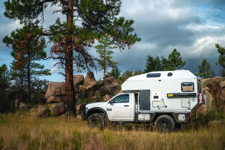 White RAM pickup truck with a hard-side slide-in truck camper in the bed, sitting level in daylight