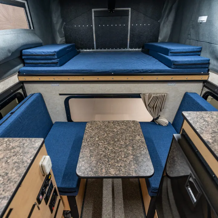 Four Wheel Camper Fleet vs Swift vs Hawk: Which Pop-Up Fits Your Truck? 3 Front-dinette interior of a Four Wheel Camper Fleet with the table raised and the cabover bed visible, daylight coming through the windows