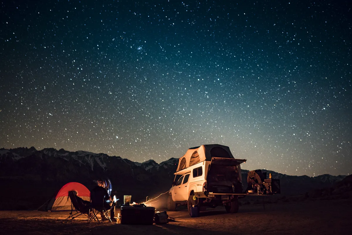 Four Wheel Camper Fleet vs Swift vs Hawk: Which Pop-Up Fits Your Truck? 6 Pop-up truck camper glowing with warm interior lights at a night campsite under a starry sky