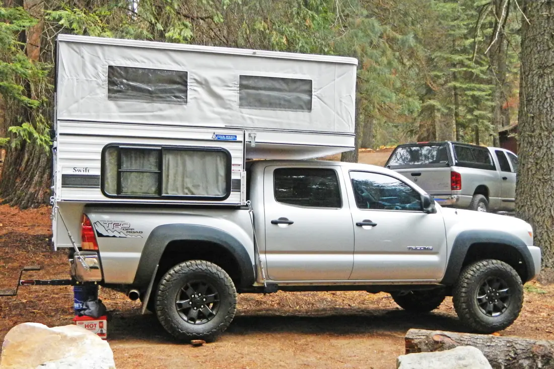 Four Wheel Camper Fleet vs Swift vs Hawk: Which Pop-Up Fits Your Truck? 2 Four Wheel Camper Swift pop-up truck camper mounted on a Toyota Tacoma crew cab with the roof popped up, parked on a forest road