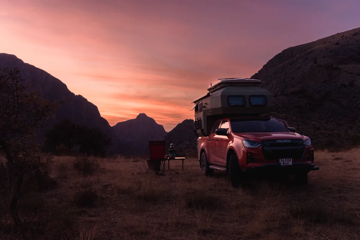 Slide-in truck camper on a pickup truck at a mountain campsite at sunset with camp chairs and gear set up.