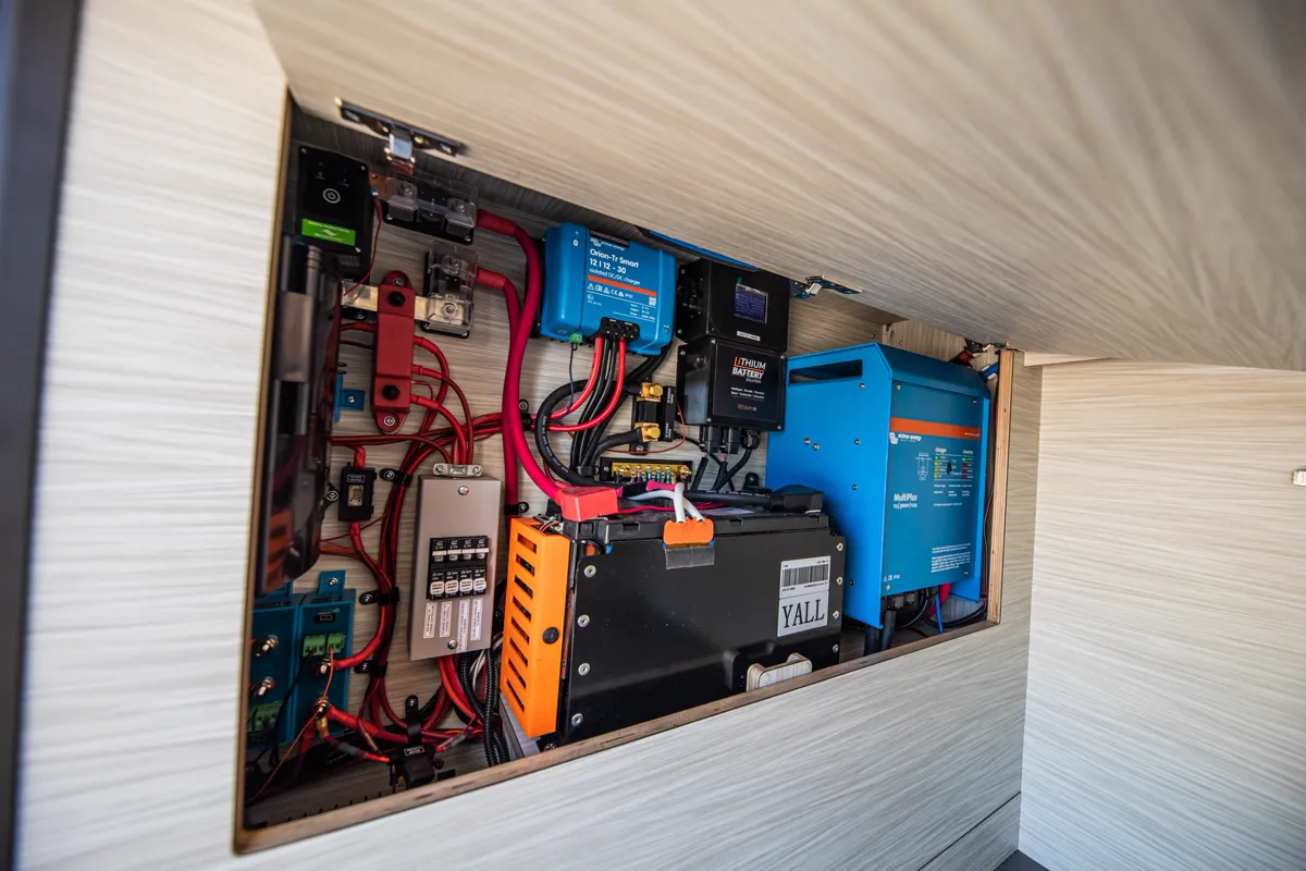 12V fuse block with labeled red and black wiring, lithium battery box, and DC-DC charger in a camper wall cavity.