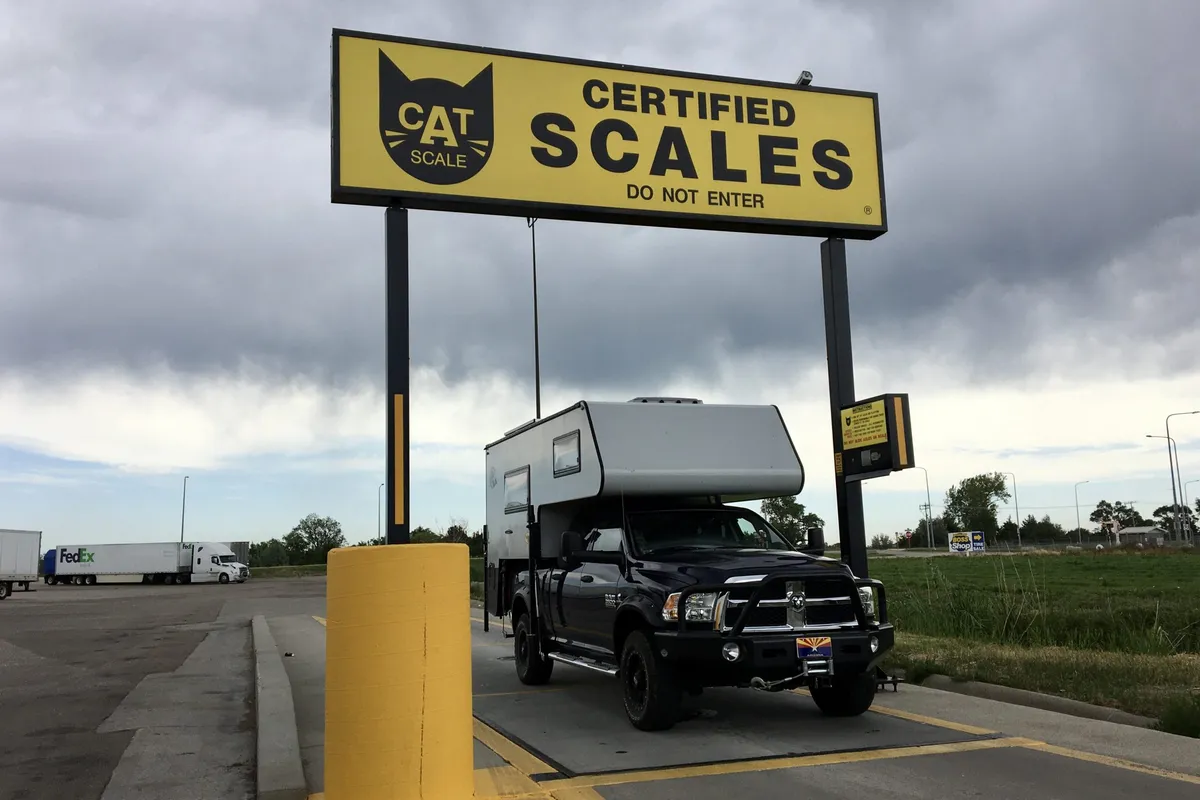 Pickup truck with slide-in camper being weighed on a CAT scale to check front and rear axle weights.