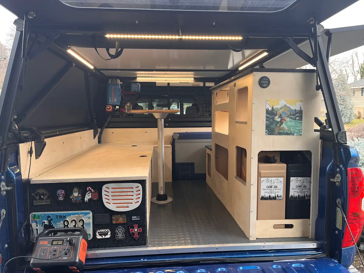 DIY plywood bed platform and cabinet boxes inside a truck camper, with a vented panel under the platform.