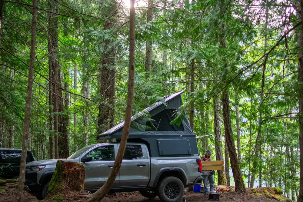 Truck Camper for Tall People: What Actually Works at 6'2" and Up 4 Pop-up truck camper with roof raised at a forest campsite