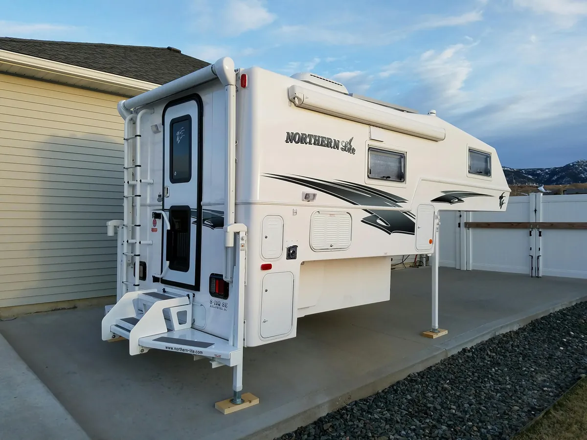 Slide-in truck camper resting on storage jacks in a residential driveway, off the truck