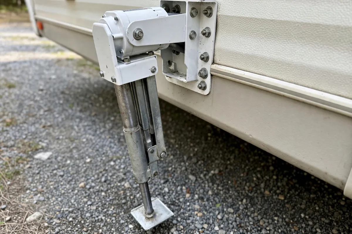 Electric corner jack partially extended on a truck camper, inner leg and bracket mount visible