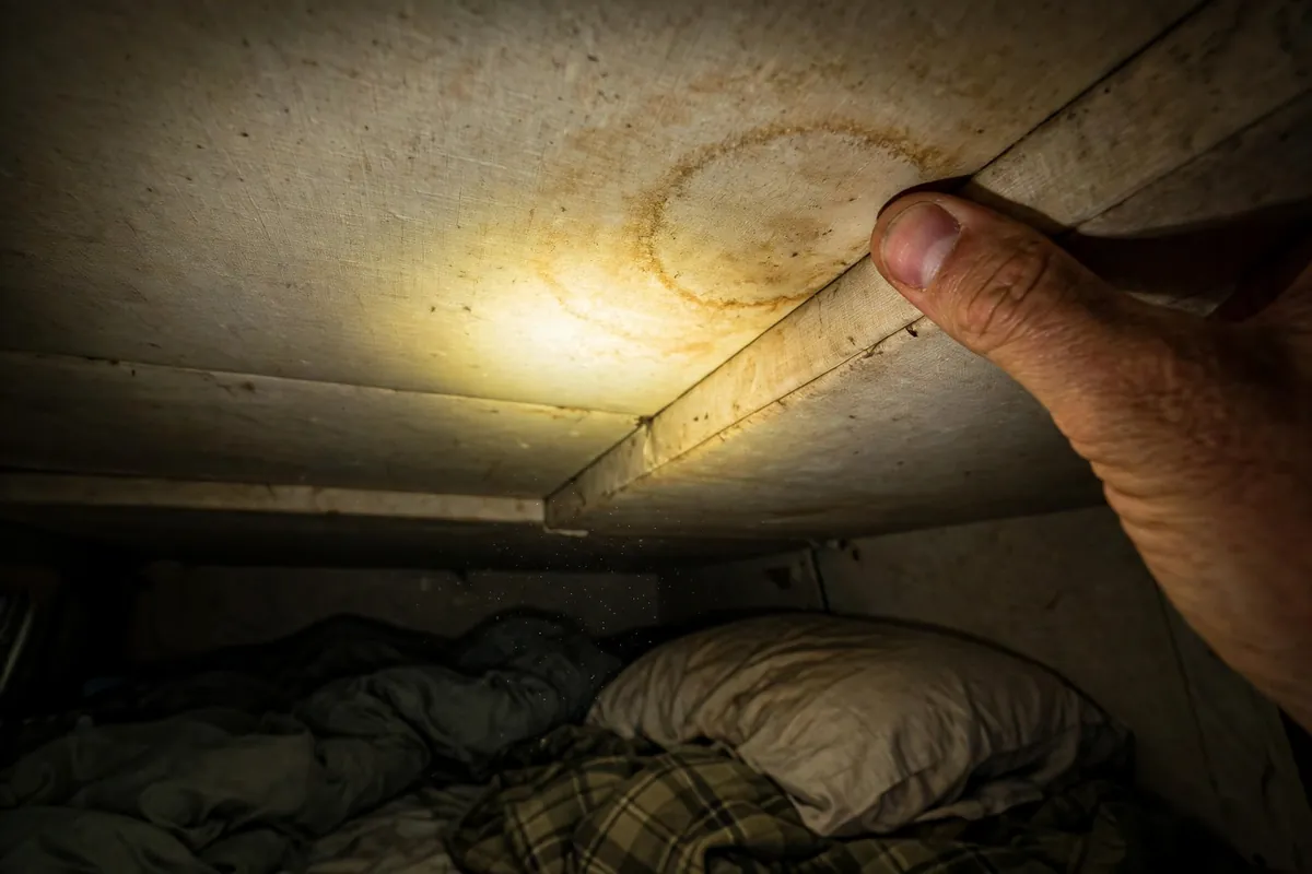 Thumb pressing into a truck camper cabover ceiling corner beside a faint brown water ring stain