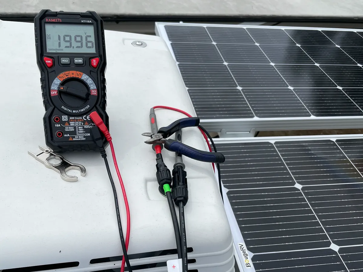 Rooftop solar panel installation on a camper with a multimeter reading panel voltage during wiring.