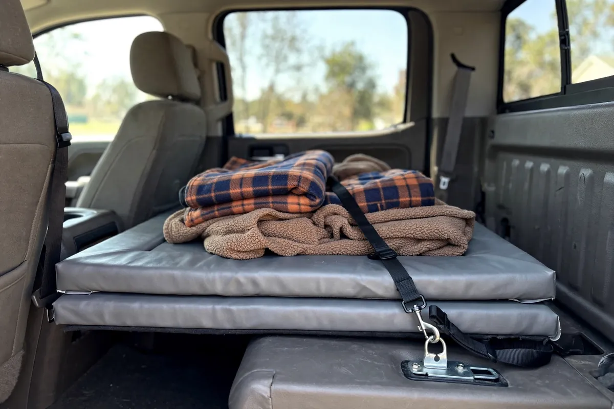 Crew cab rear bench folded flat with a vinyl-covered foam pad, dog blankets, and a harness tether