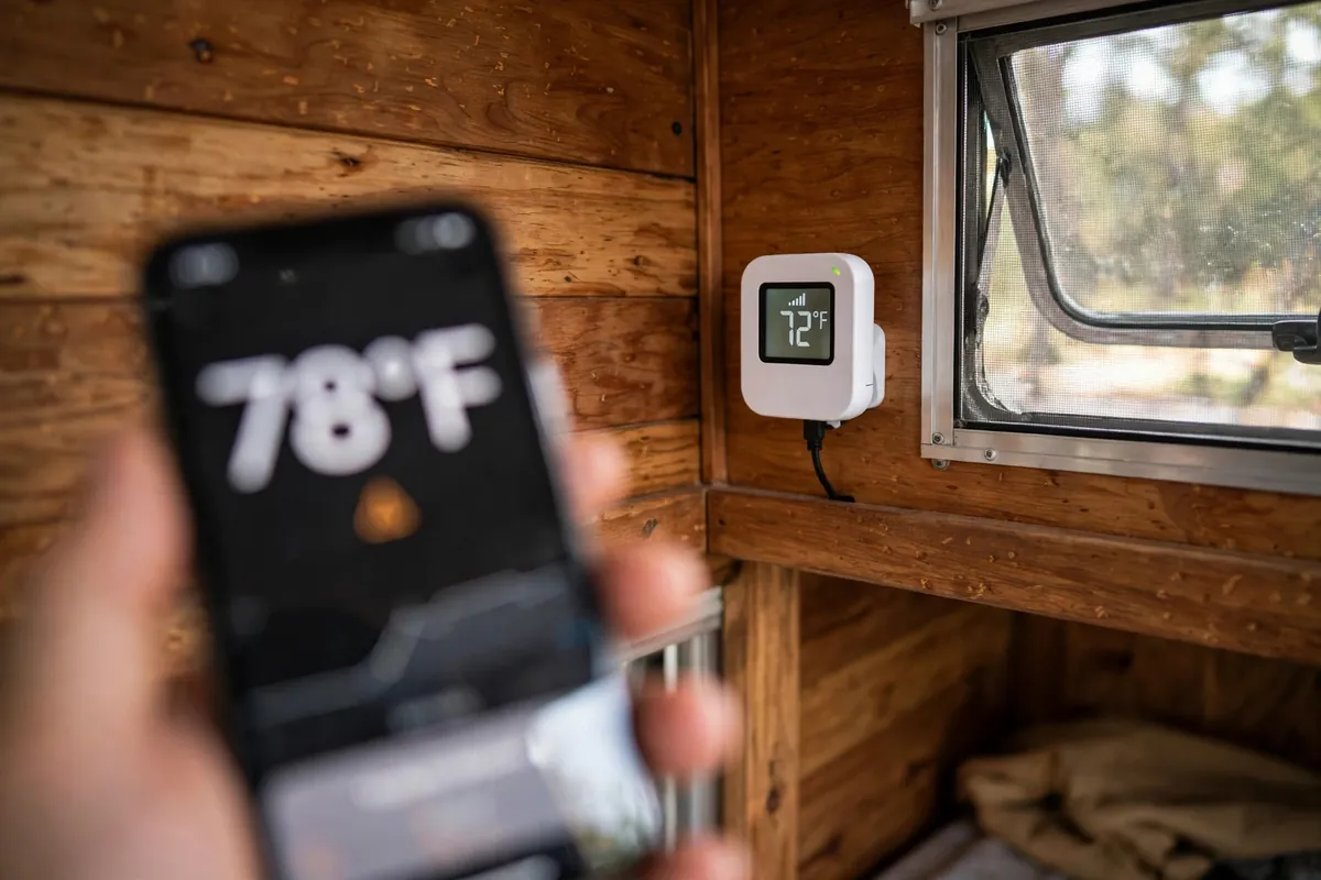Cellular pet temperature monitor mounted on a camper wall with a phone showing a temperature alert