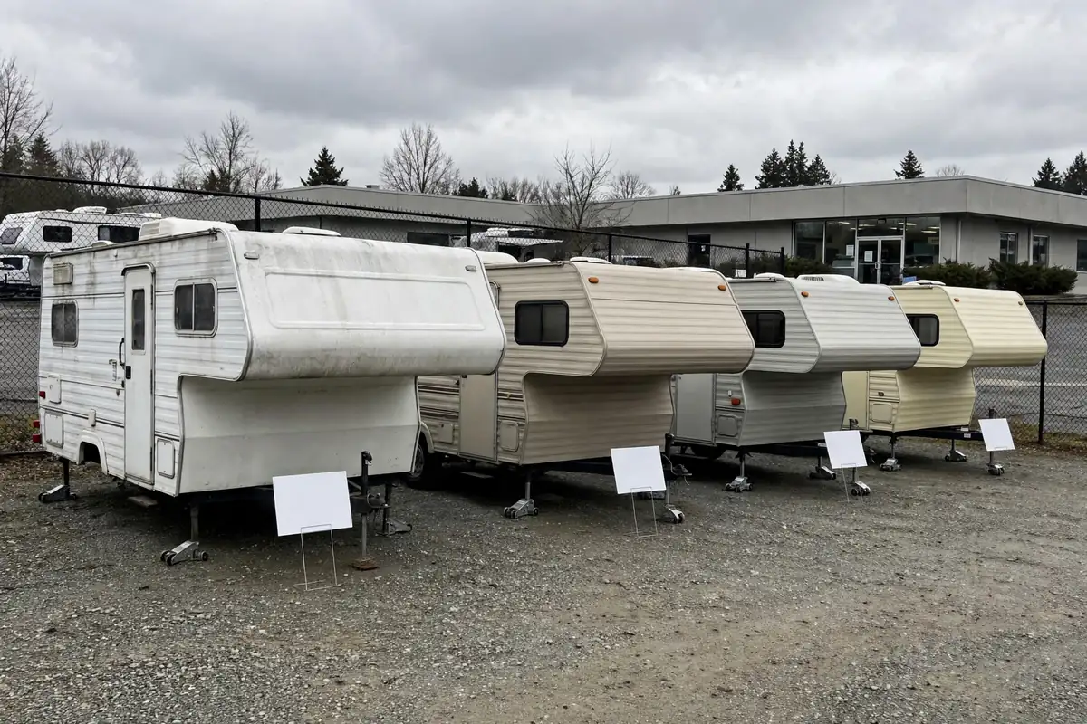 Truck Camper Cost Per Year: The True Cost of Ownership 2 Row of used slide-in truck campers for sale on a dealer lot, price placards on display, overcast daylight