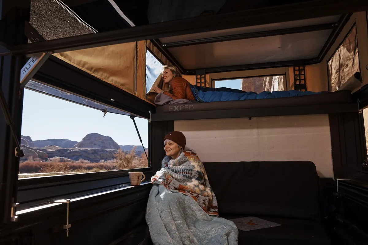 Tune M1 Pop-Up Truck Camper Review: 2026 Hands-On Verdict 7 Two people relaxing inside the Tune M1 with the bed deployed and desert views