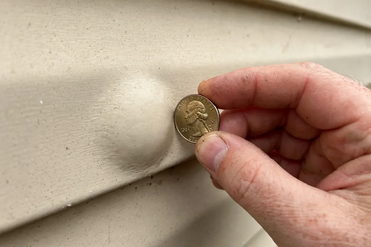 Hand tapping a truck camper sidewall with a coin next to a delamination bubble during the tap test